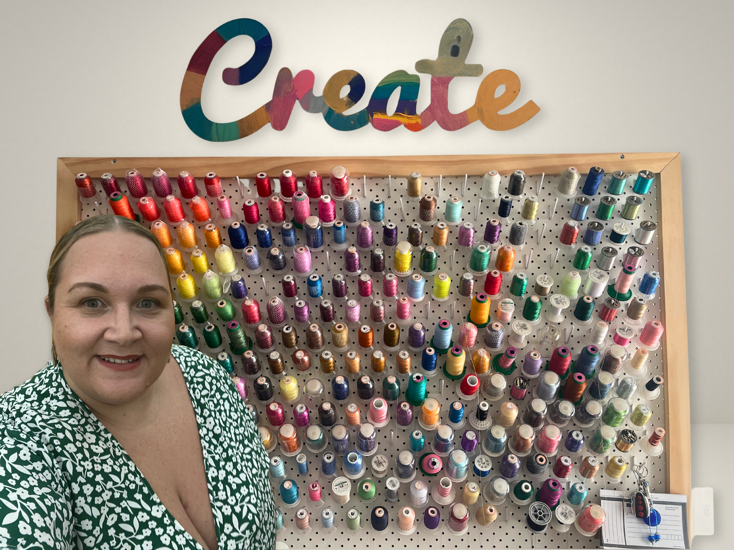 Woman standing next to a pegboard with colorful thread spools and a 'Create' sign on a white wall.