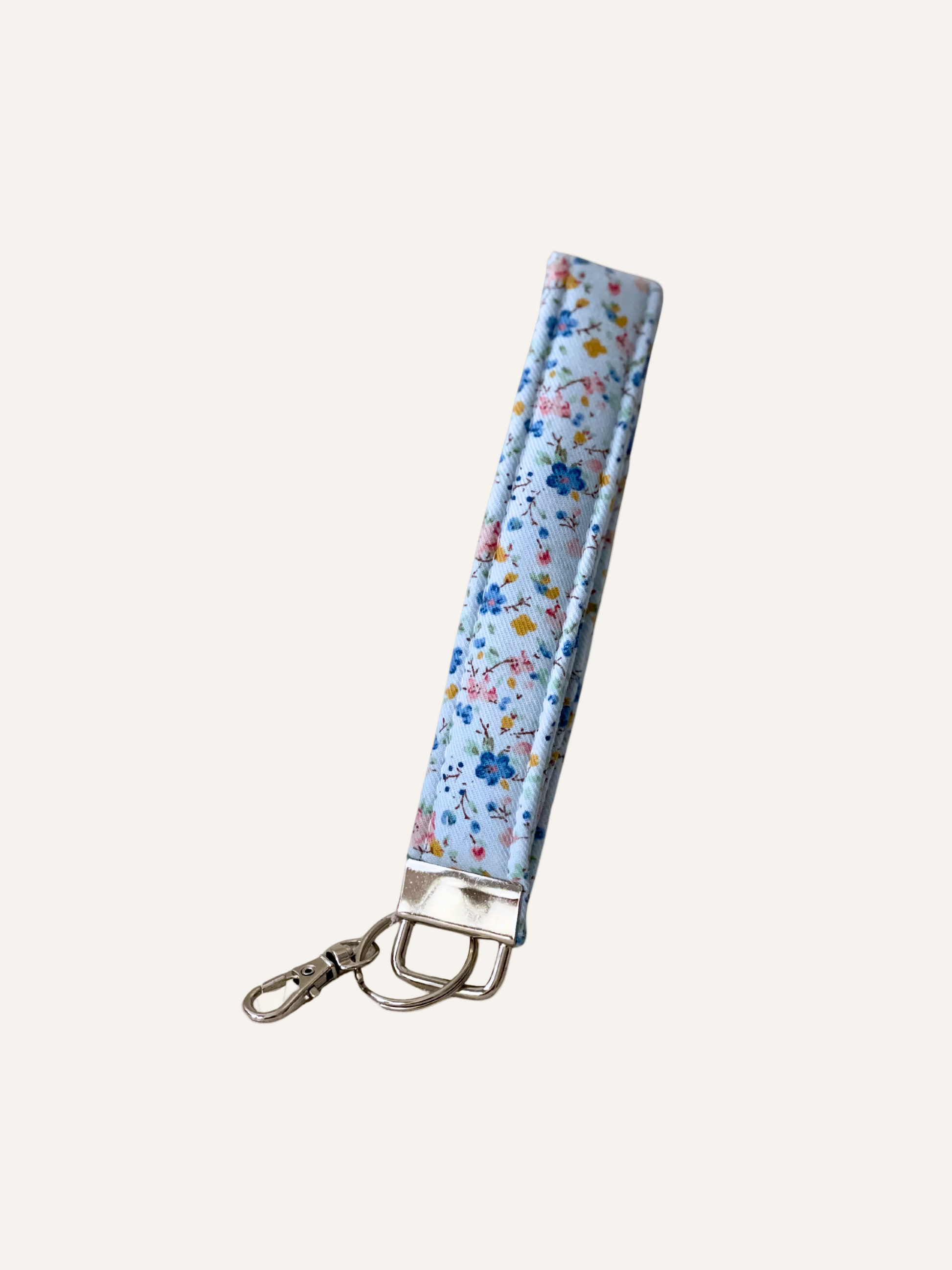 a padded fabric keyring wristlet in soft light blue with ditsy blue and pink florals on a warm cream background.