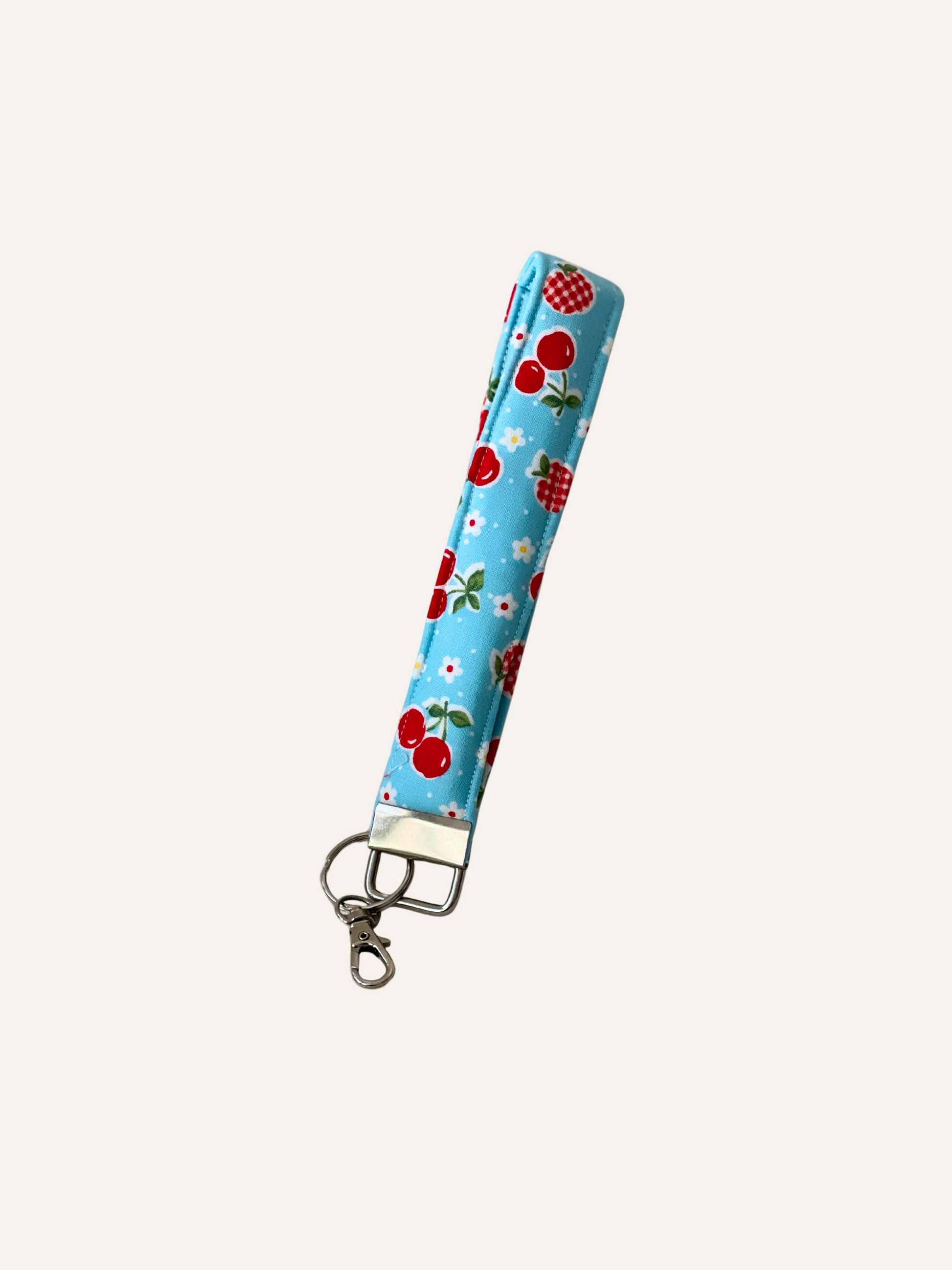 a padded keyring wristlet in a cherries and gingham apples print on sky blue fabric on a warm cream background