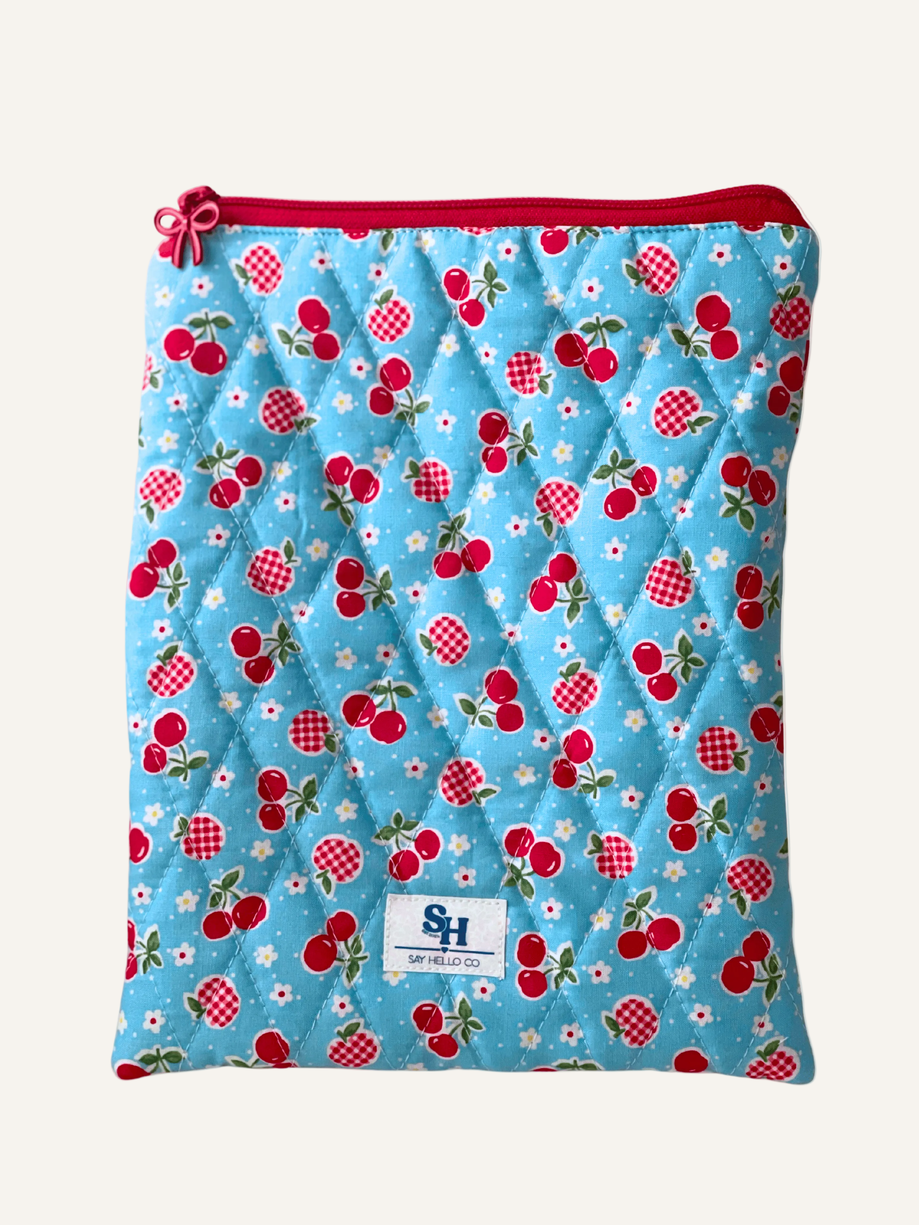 Quilted book sleeve with cherry and gingham apple pattern on sky blue fabric on a warm cream background