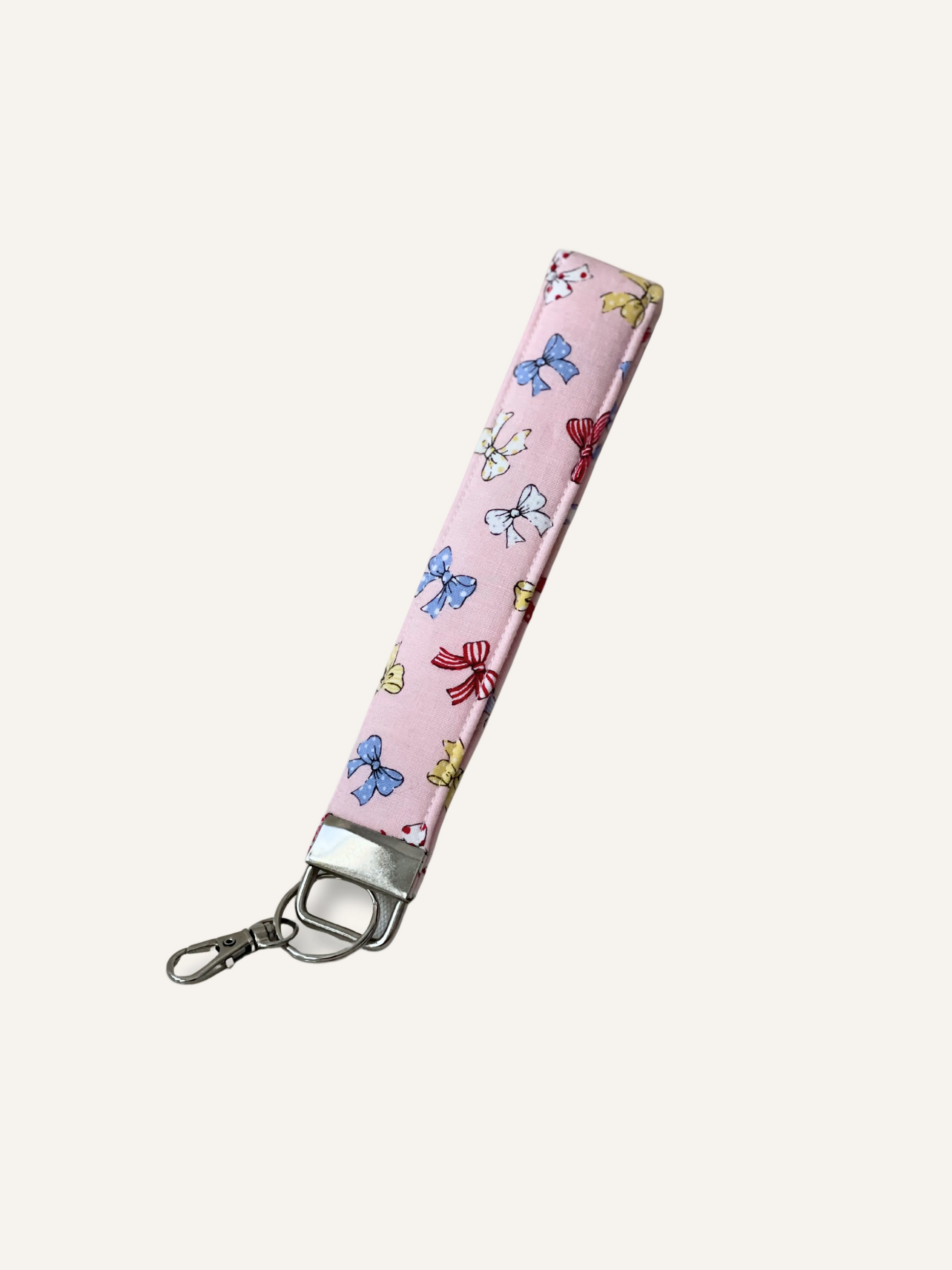a padded keyring wristlet in pink with tiny colourful bows fabric on a warm cream backround