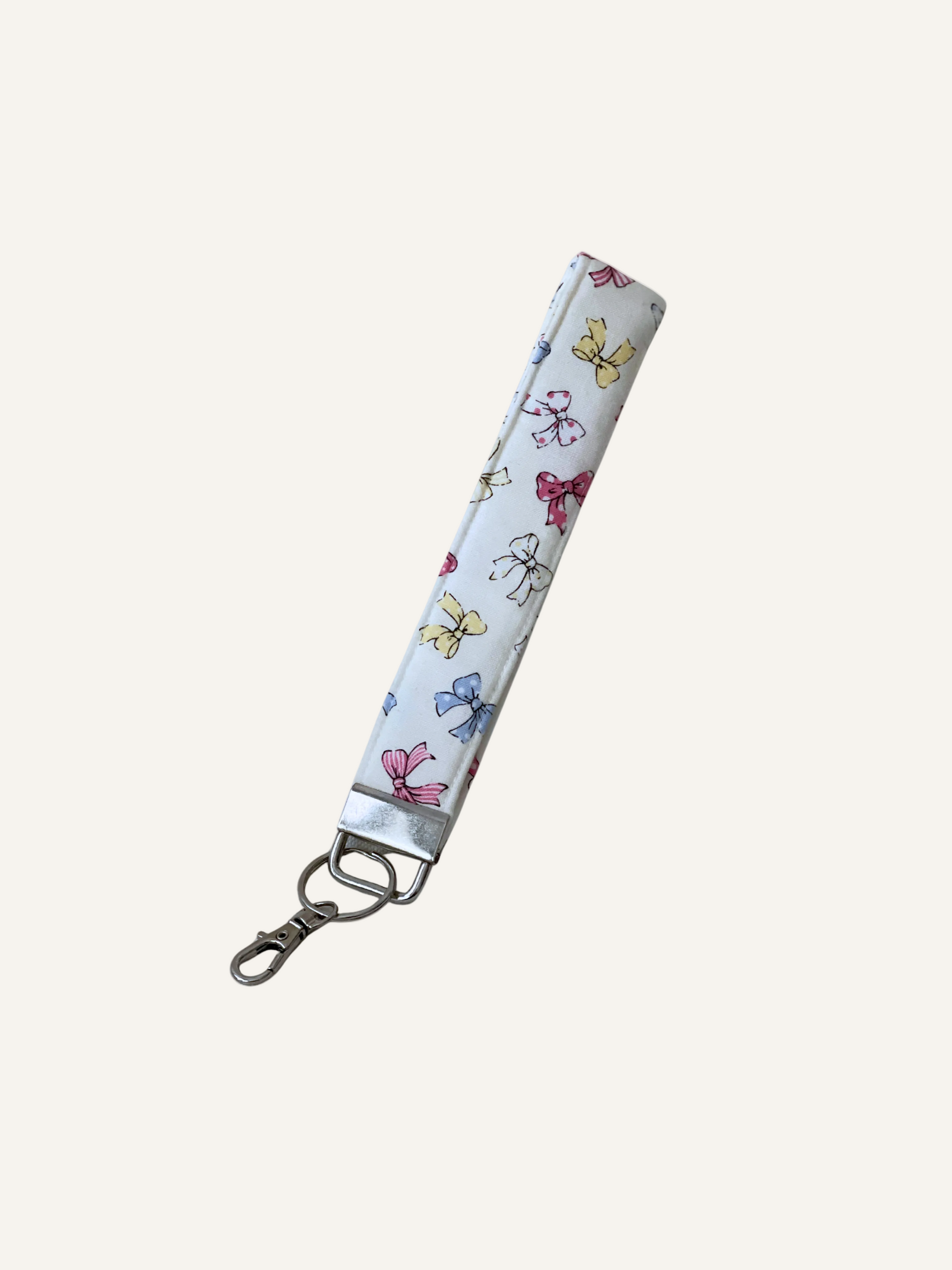 a padded fabric keyring wristlet in cream with tiny colourful bows pattern on a warm cream background