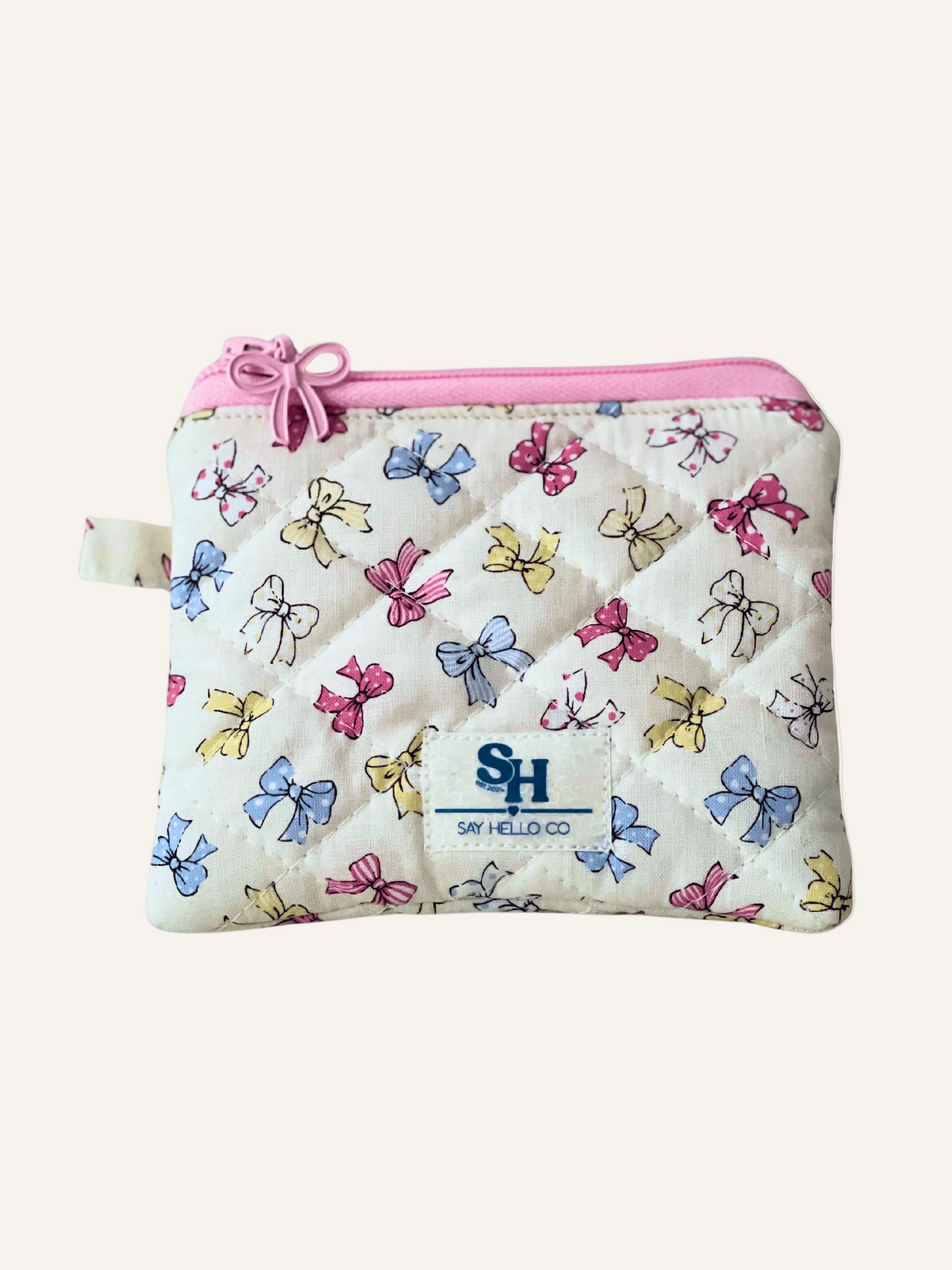 Small zippered pouch with colorful bow pattern and pink zipper and bow on a warm cream background