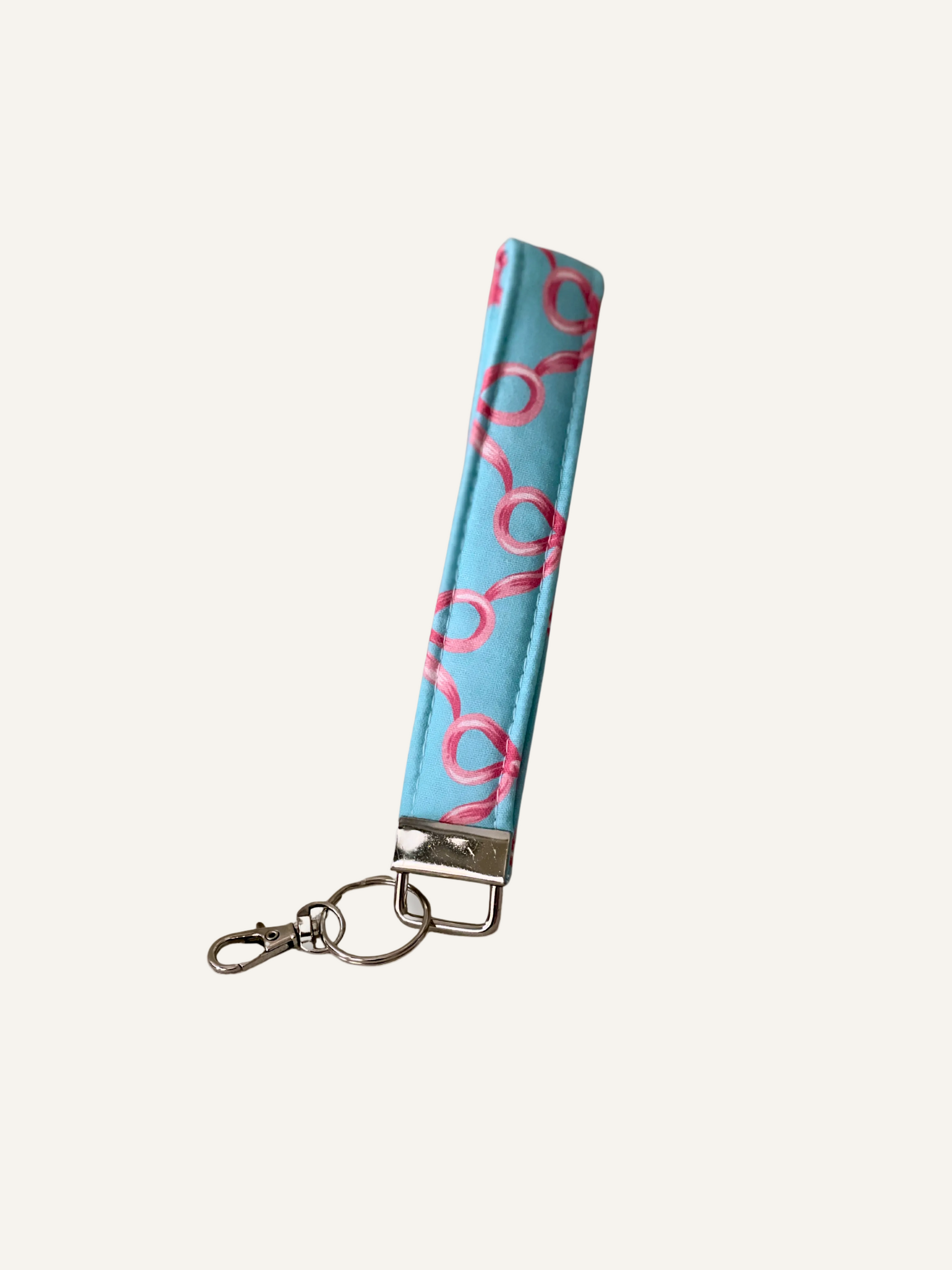 Keychain wristlet with padded fabric blue strap featuring pink bow patterns on a warm cream background