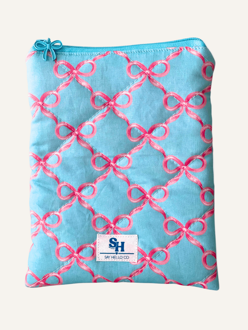 a quilted book sleeve in light blue with pink bows and a blue bow zipper on a warm cream background