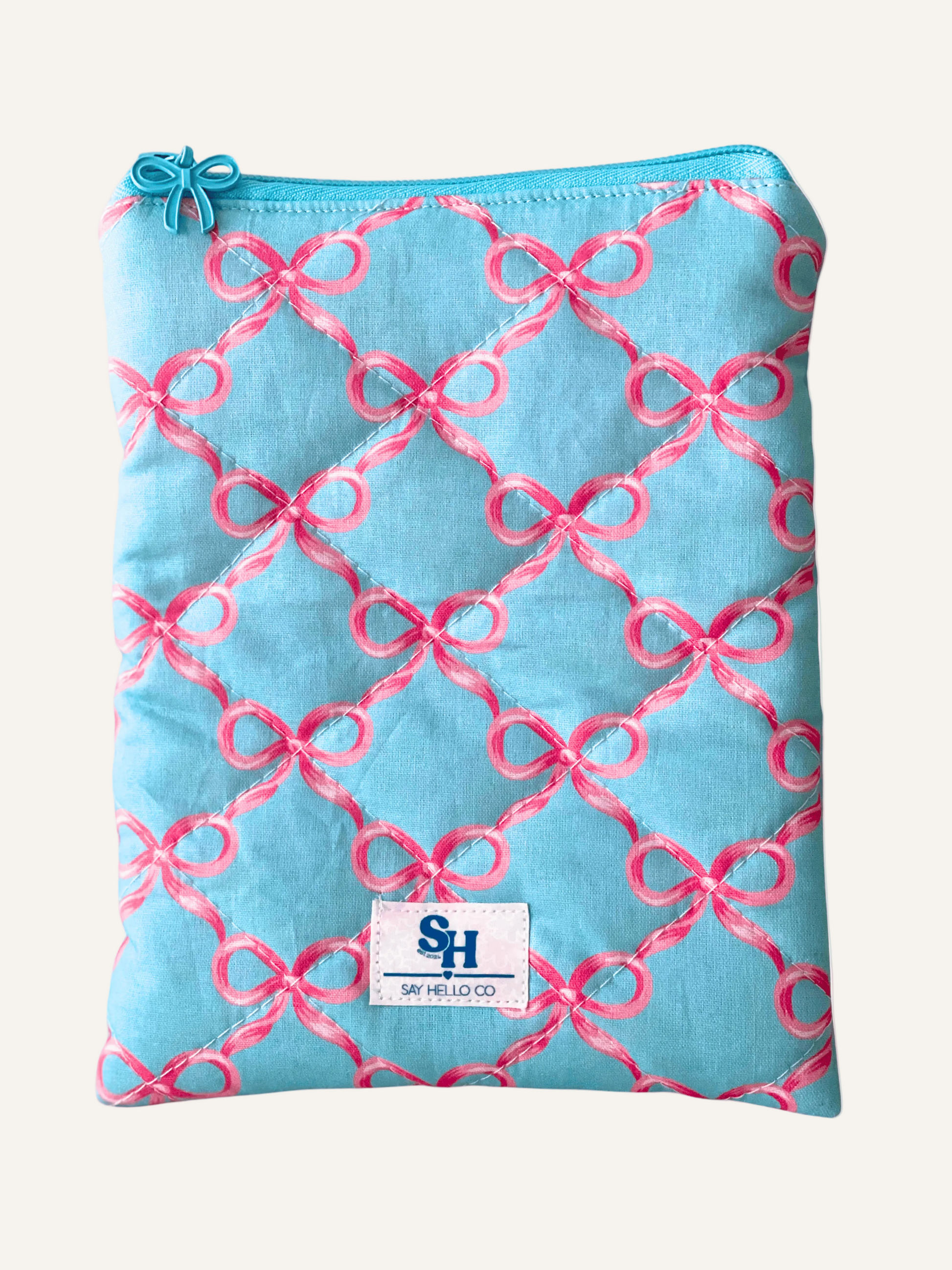 a quilted book sleeve in light blue with pink bows and a blue bow zipper on a warm cream background
