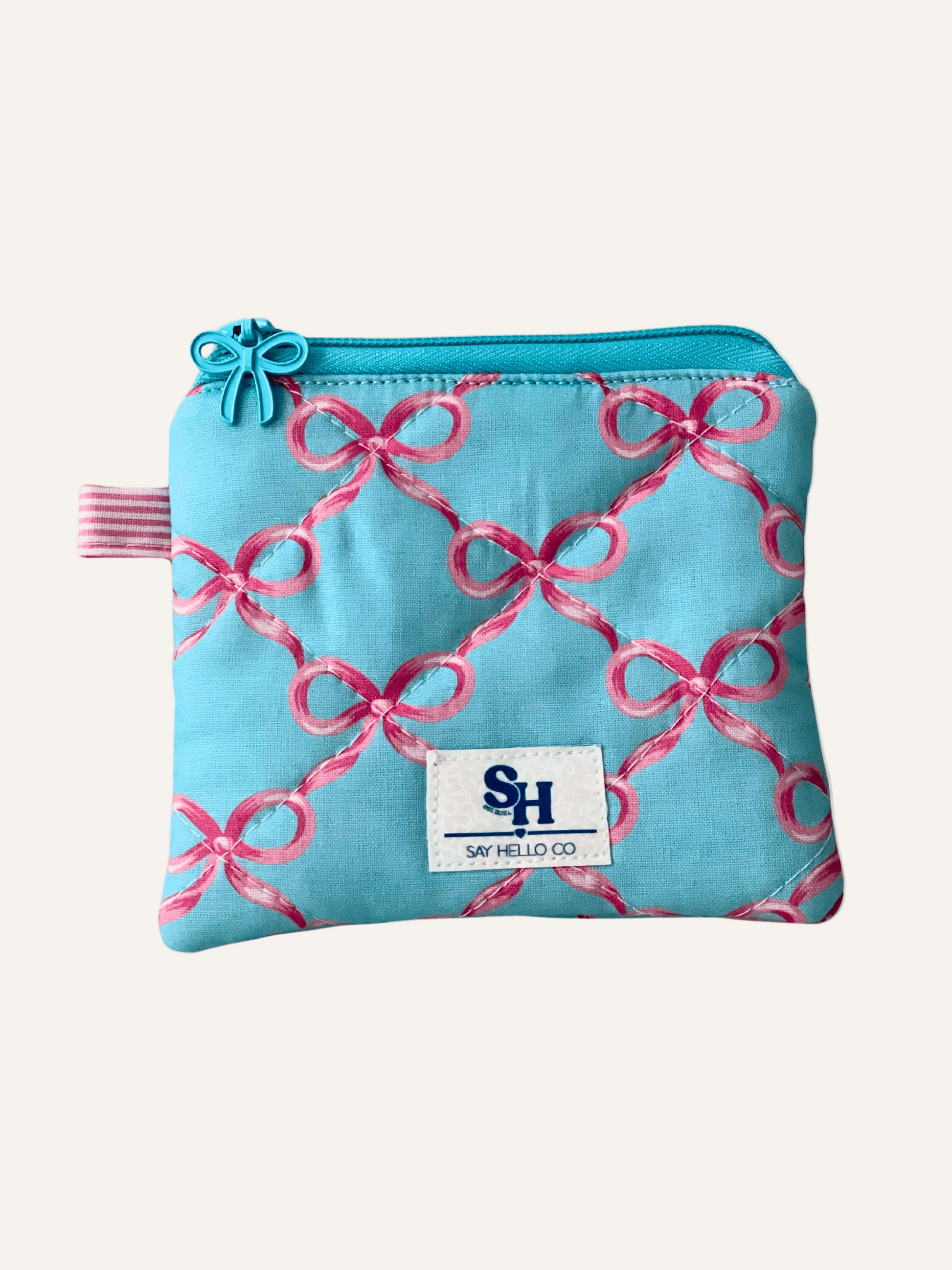 small light blue zippered pouch with pink bows as the pattern, visible label, diamond quilted design on a cream background