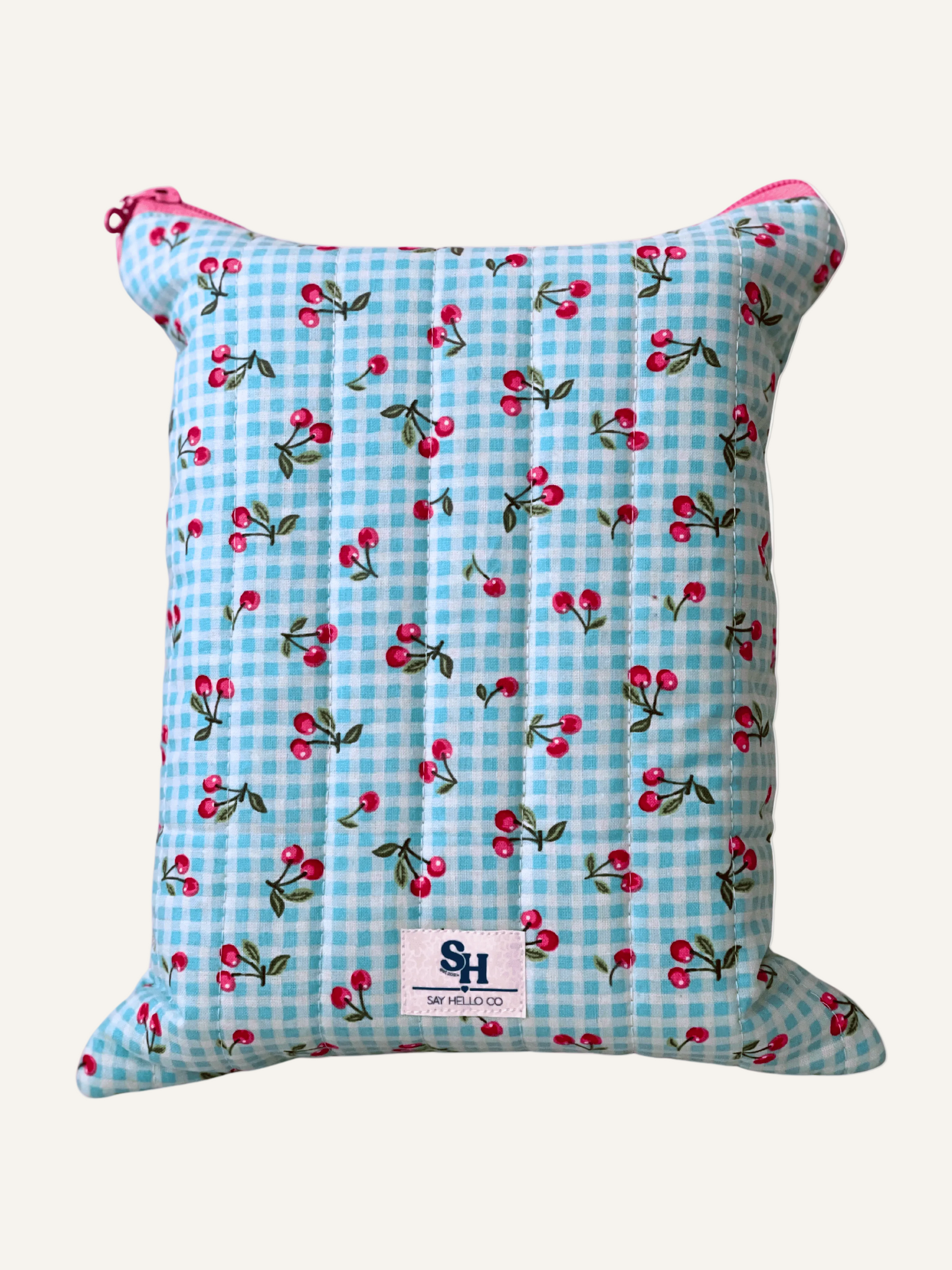 a quilted book sleeve in blue gingham with pink cherries and pink pinstripe lining and a pink bow zipper