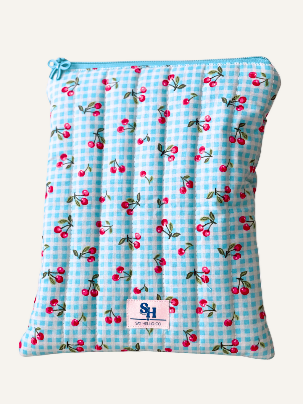 Quilted fabric booksleeve with blue gingham and pink cherry pattern on a warm cream background