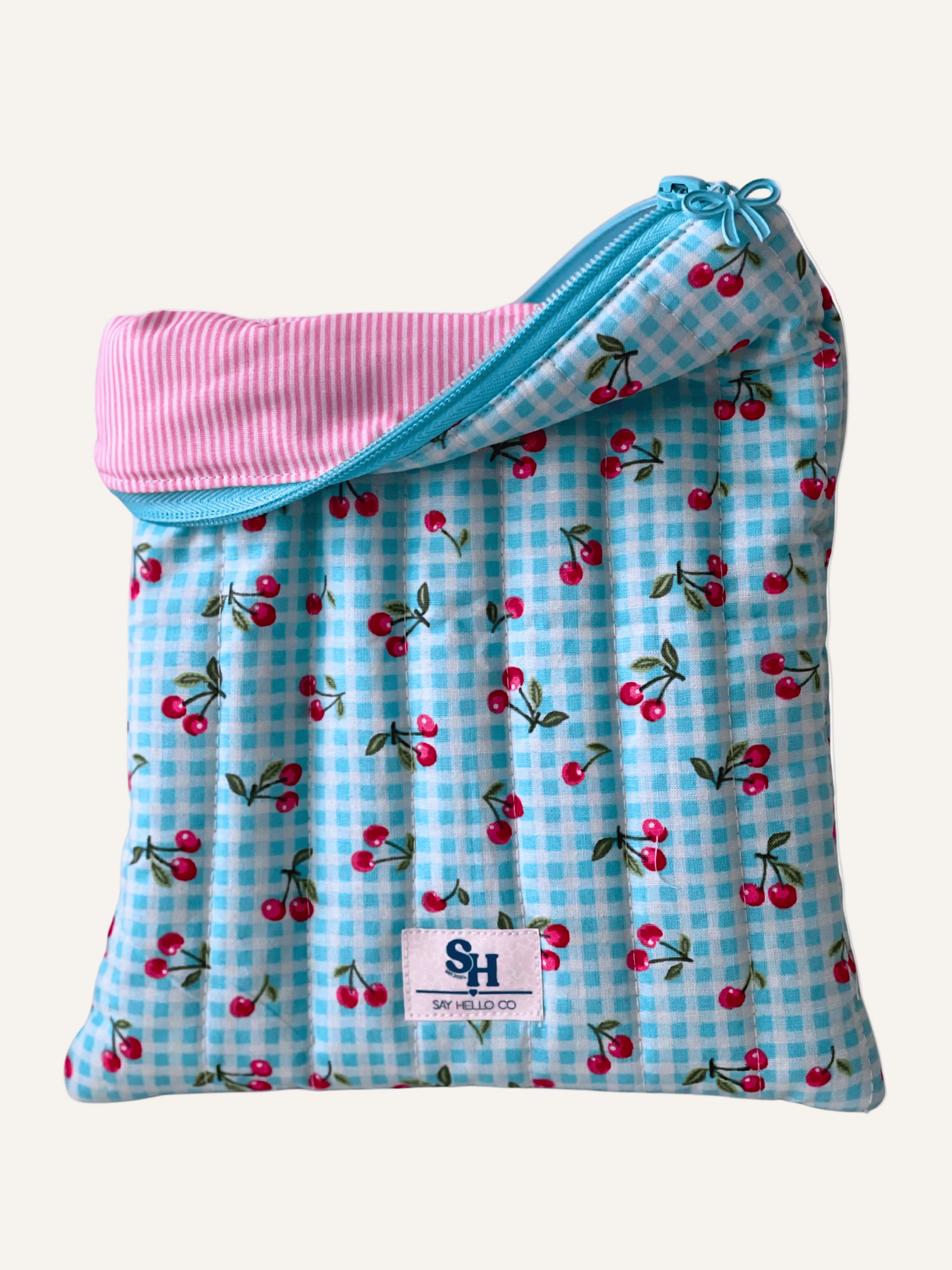quilted booksleeve with cherry pattern and pink and white pinstripe lining on a warm cream background