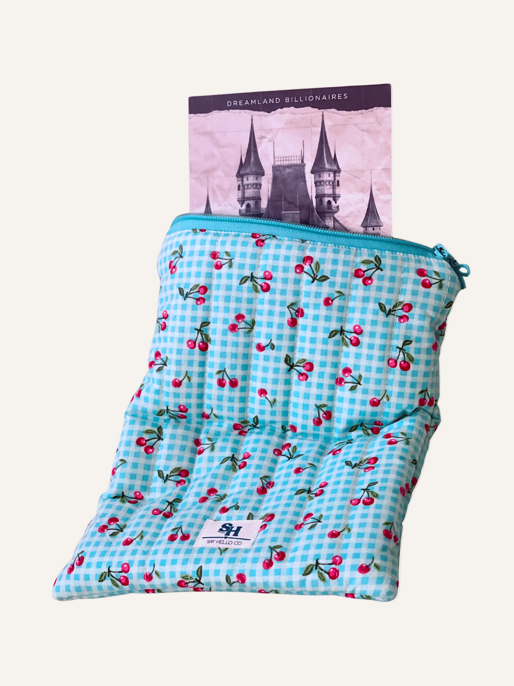 Blue gingham bag with cherry pattern containing a book on a warm cream background
