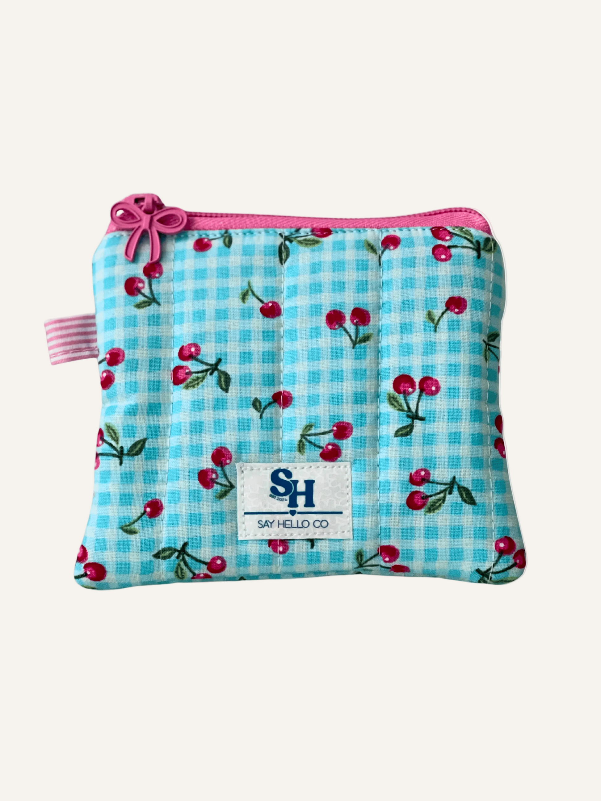 a quilted mini wallet in blue gingham with pink cherries fabric and a pink bow zipper on a warm cream background