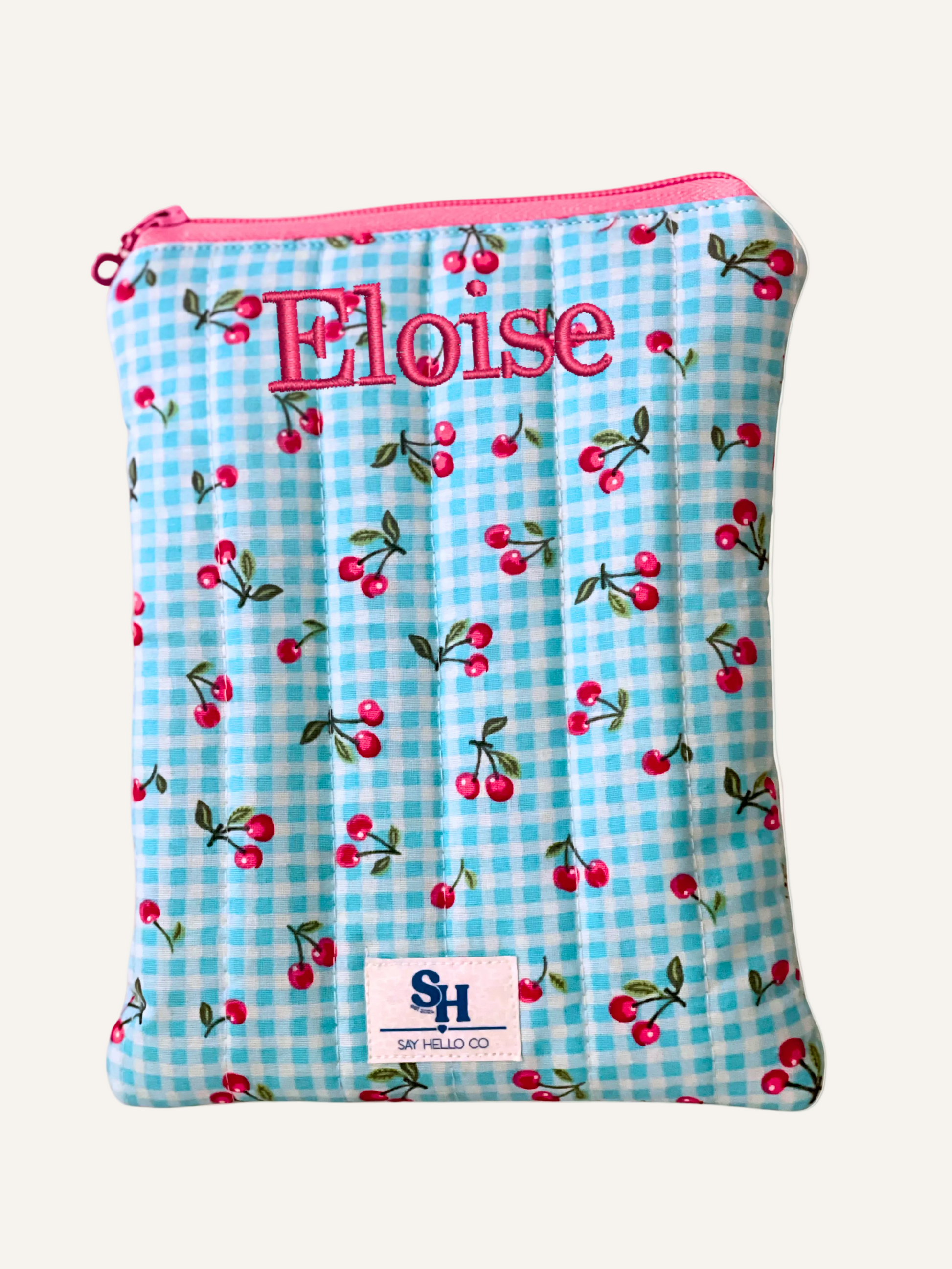 Blue gingham and pink cherry patterned quilted fabric booksleeve with "Eloise" embroidered in pink