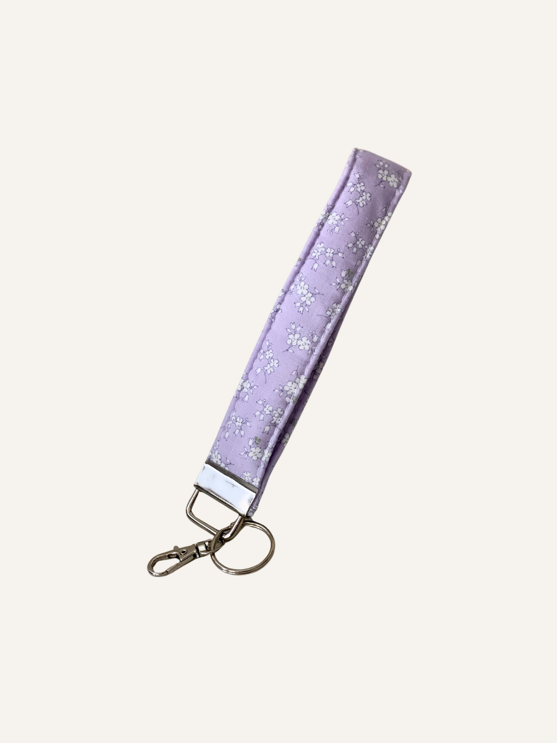 a padded keyring wristlet in light lilac with delicate white flowers patterned fabric on a warm cream background