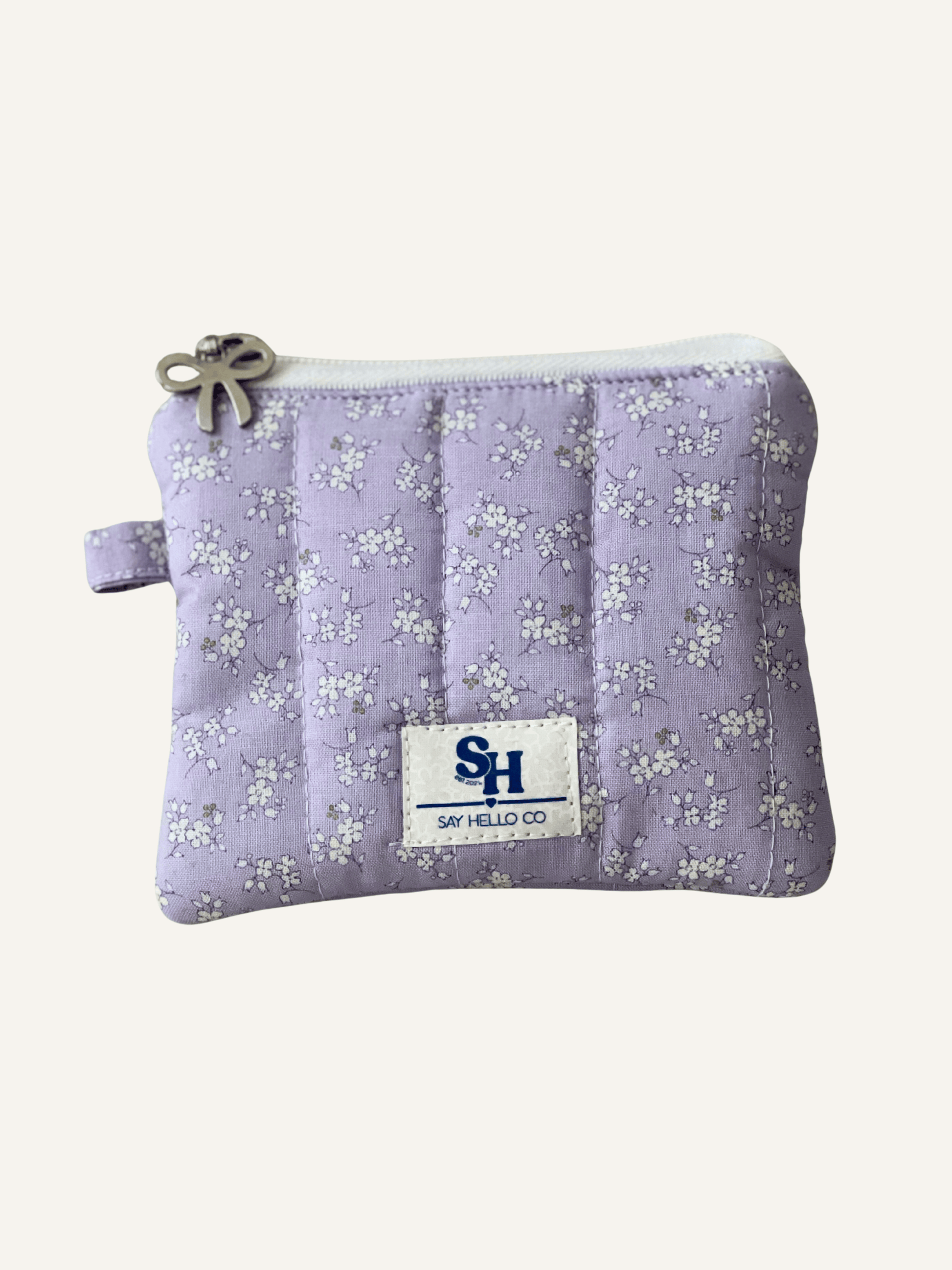Light lavender with ditsy white floral pattern zippered  pouch with a visible brand label on a warm cream background