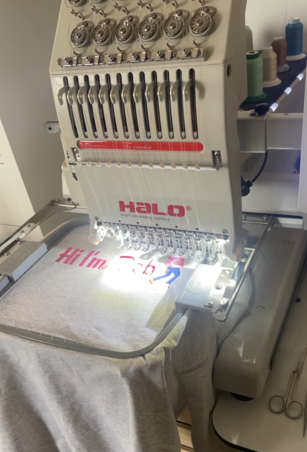 Embroidery machine with a partially embroidered shirt on a table.