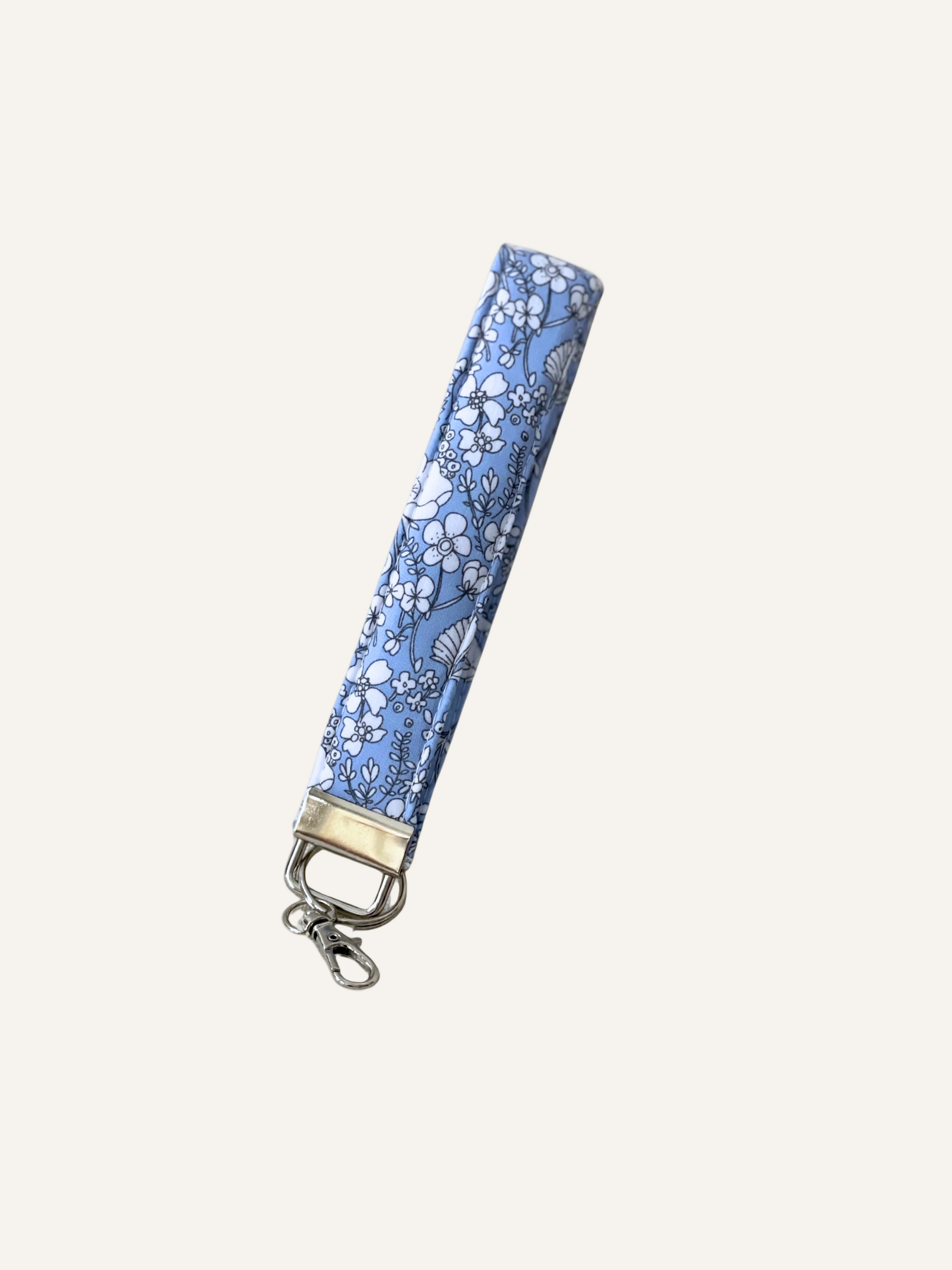 a padded fabric keyring wristlet in light blue with line drawn white flowers on a warm cream background