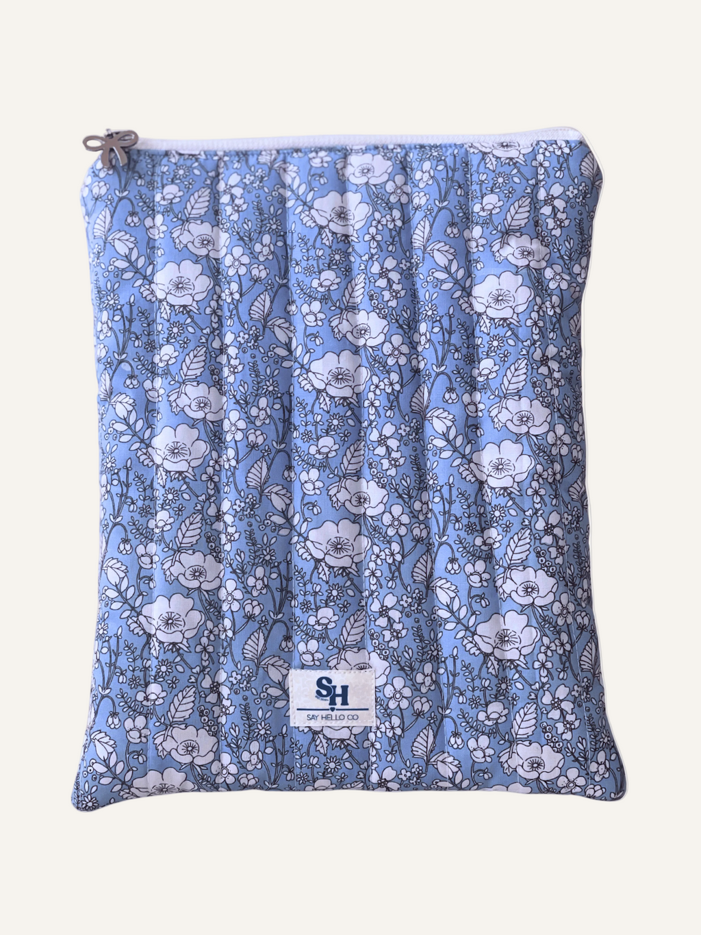 a quilted book sleeve in light blue with white flowers outlined in fine black lines with a silver bow and a visible brand lave on a warm cream background