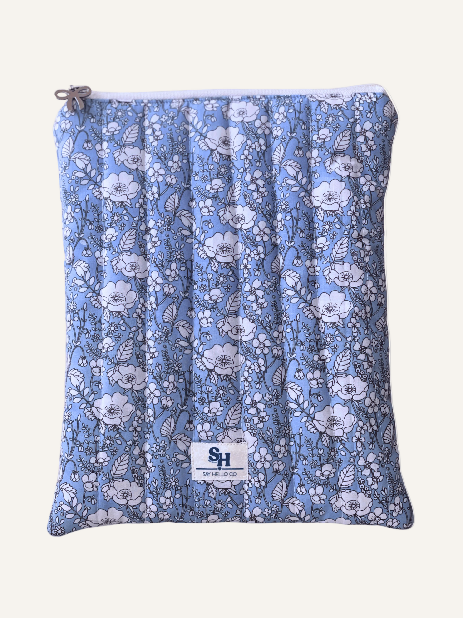 a quilted book sleeve in light blue with white flowers outlined in fine black lines with a silver bow and a visible brand lave on a warm cream background