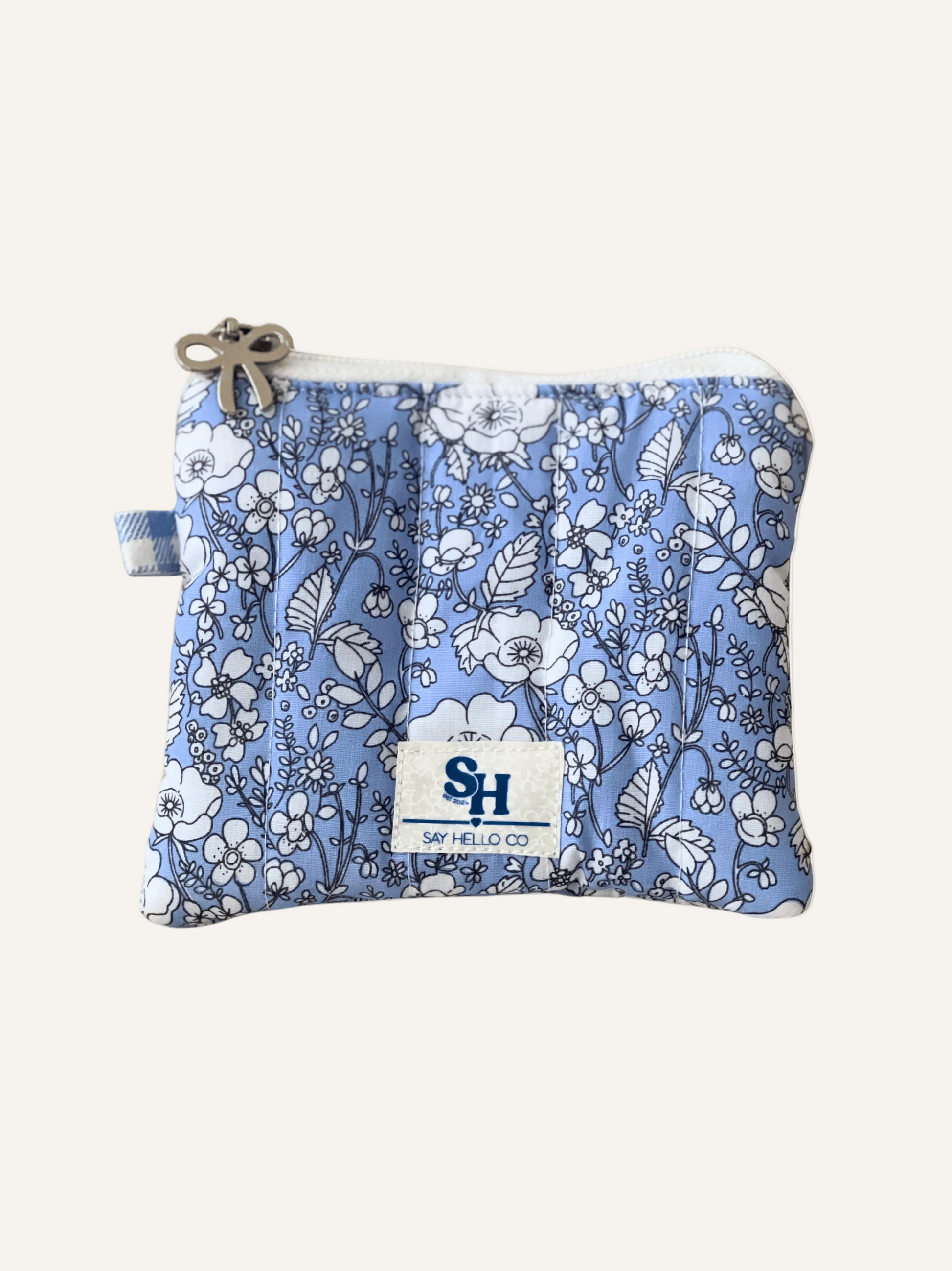 Blue with a white floral-pattern zippered pouch with a visible brand label on a warm cream background