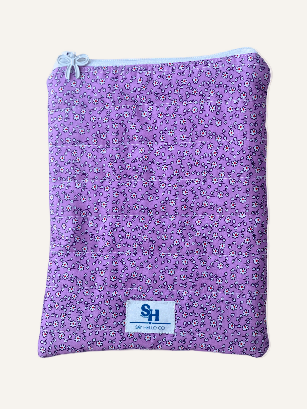 a quilted Kindle sleeve in purple floral with tiny white flowers with a white zipper and bow zipper pull on a warm cream background