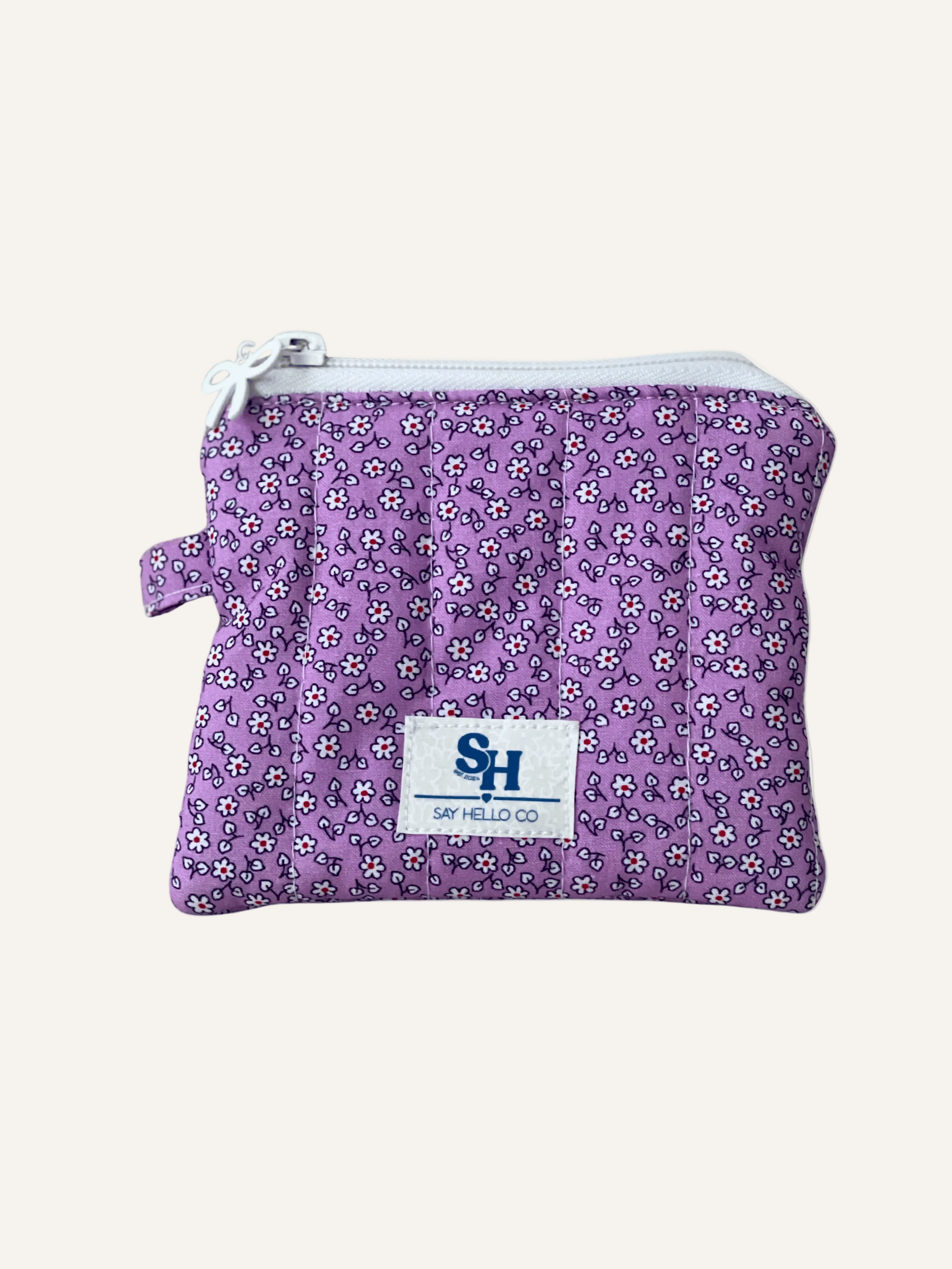 Purple and white floral-patterned pouch with a visible brand logo on a warm cream background