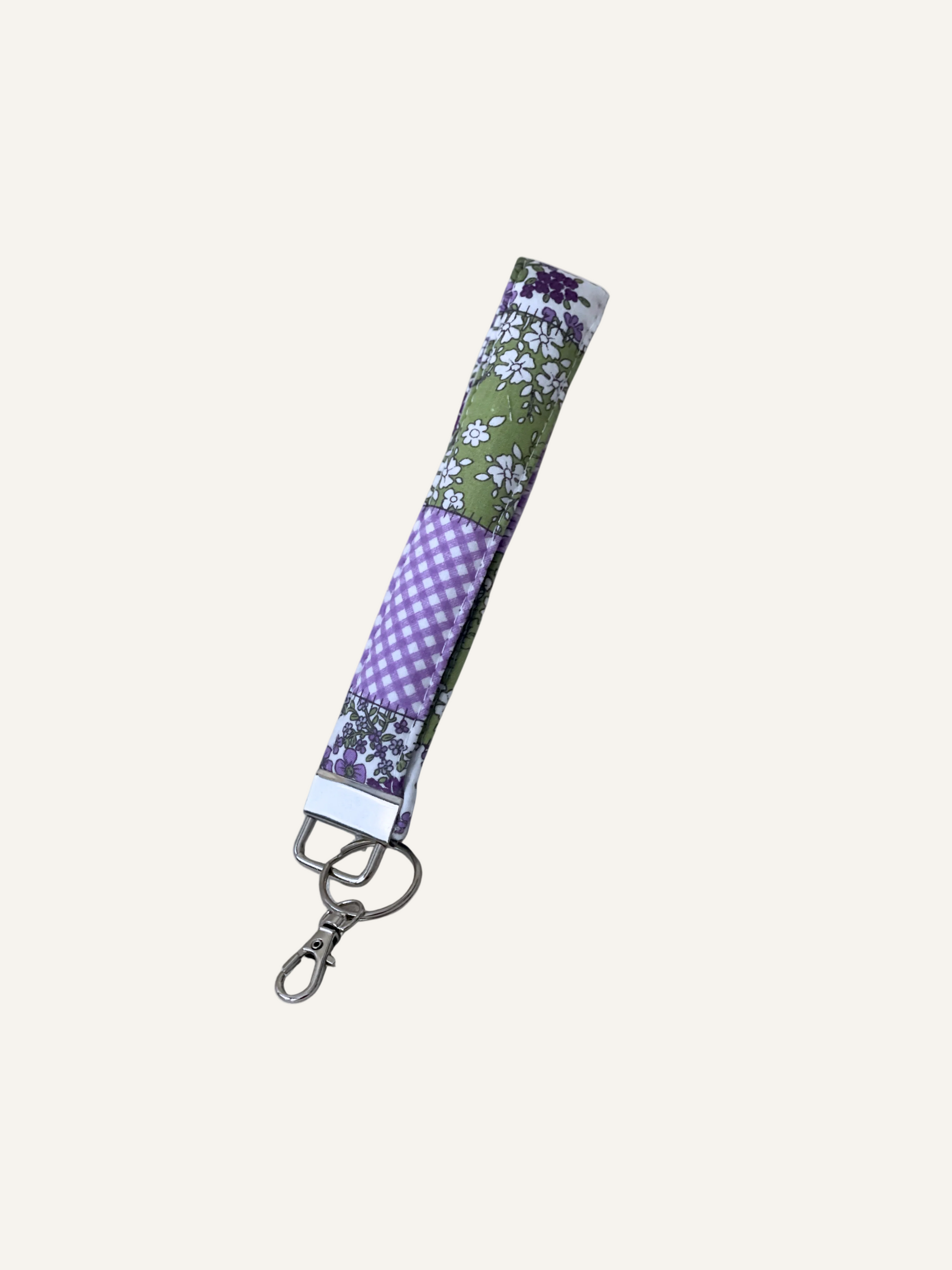 a padded keyring wristlet in green and purple floral patchwork design fabric on a warm cream background