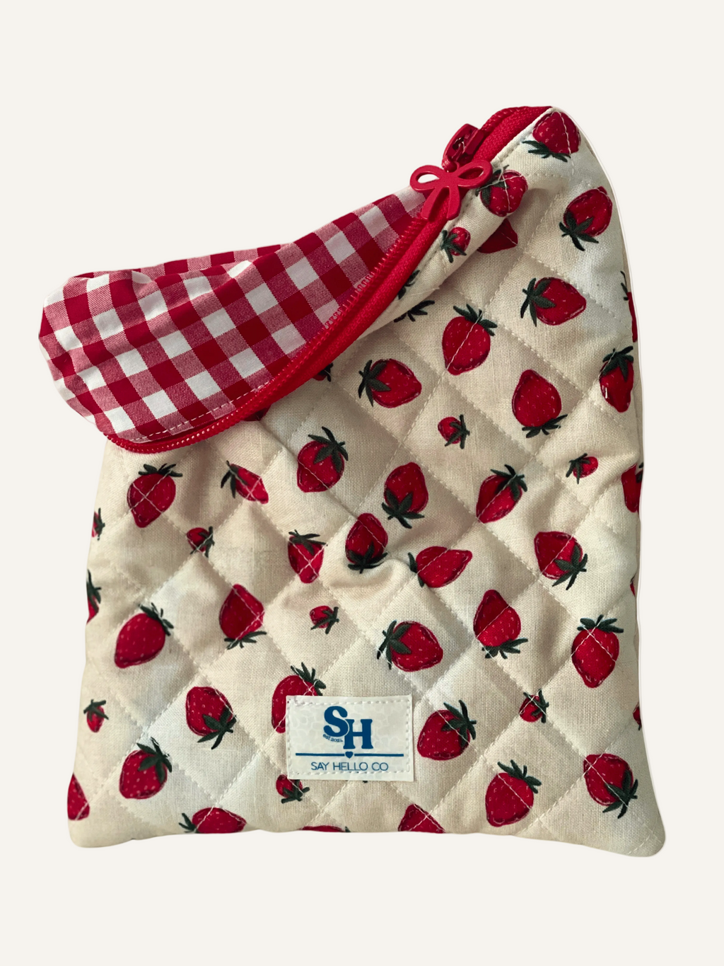 quilted book sleeve in strawberry print on cream with red bow zipper, red gingham lining and a visible brand label on a warm cream 