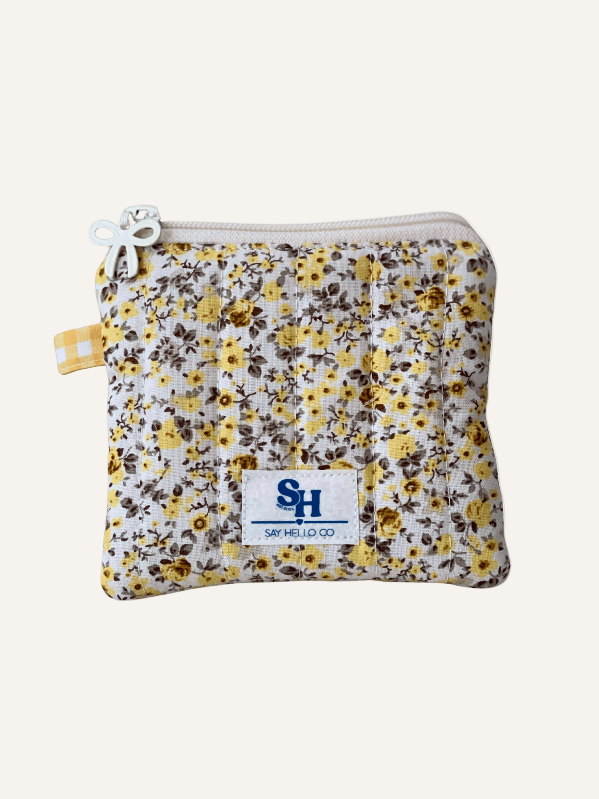 Yellow and grey beige ditsy floral-patternon cream backing pouch with a visible brand label on a warm cream background