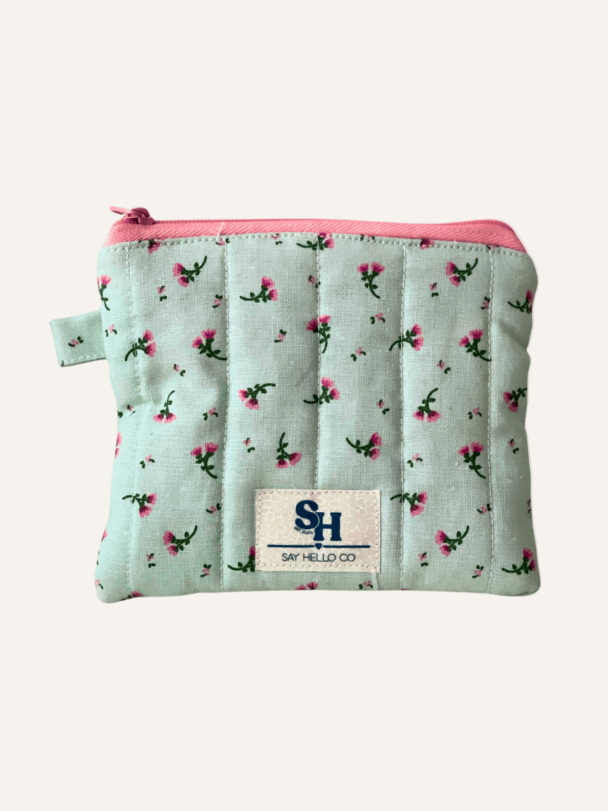 Small quilted pouch with a green and pink floral pattern and pink zipper on a beige background