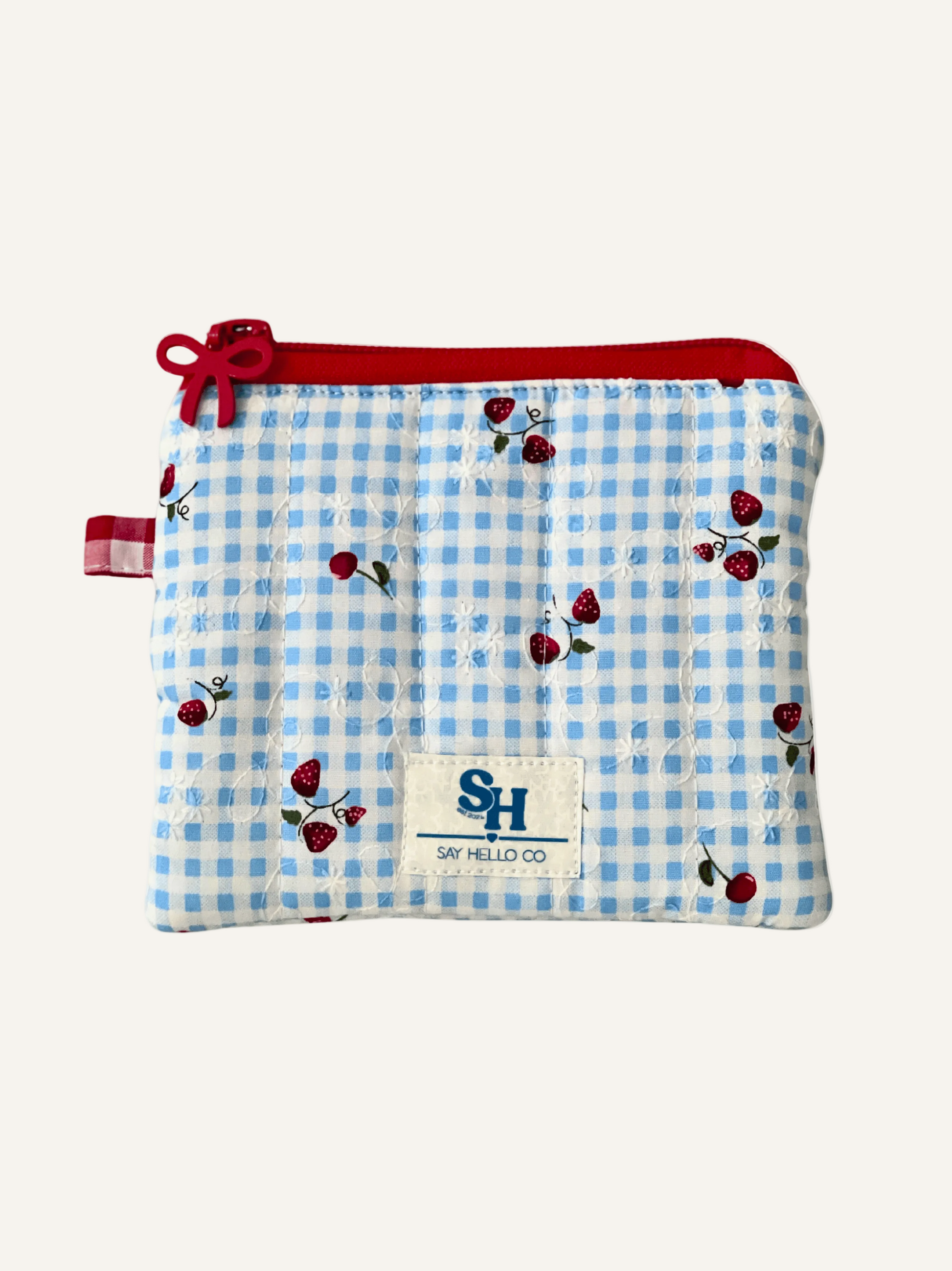 Blue gingham pouch with red bow zipper with strawberries and cherries and a visible brand label on a warm cream background