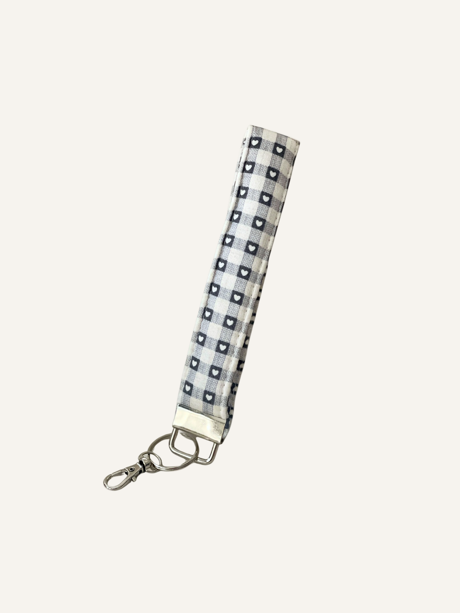 a padded fabric keyring wristlet in grey and cream gingham, tiny white hearts in the grey squares of the gingham pattern. on a warm cream background