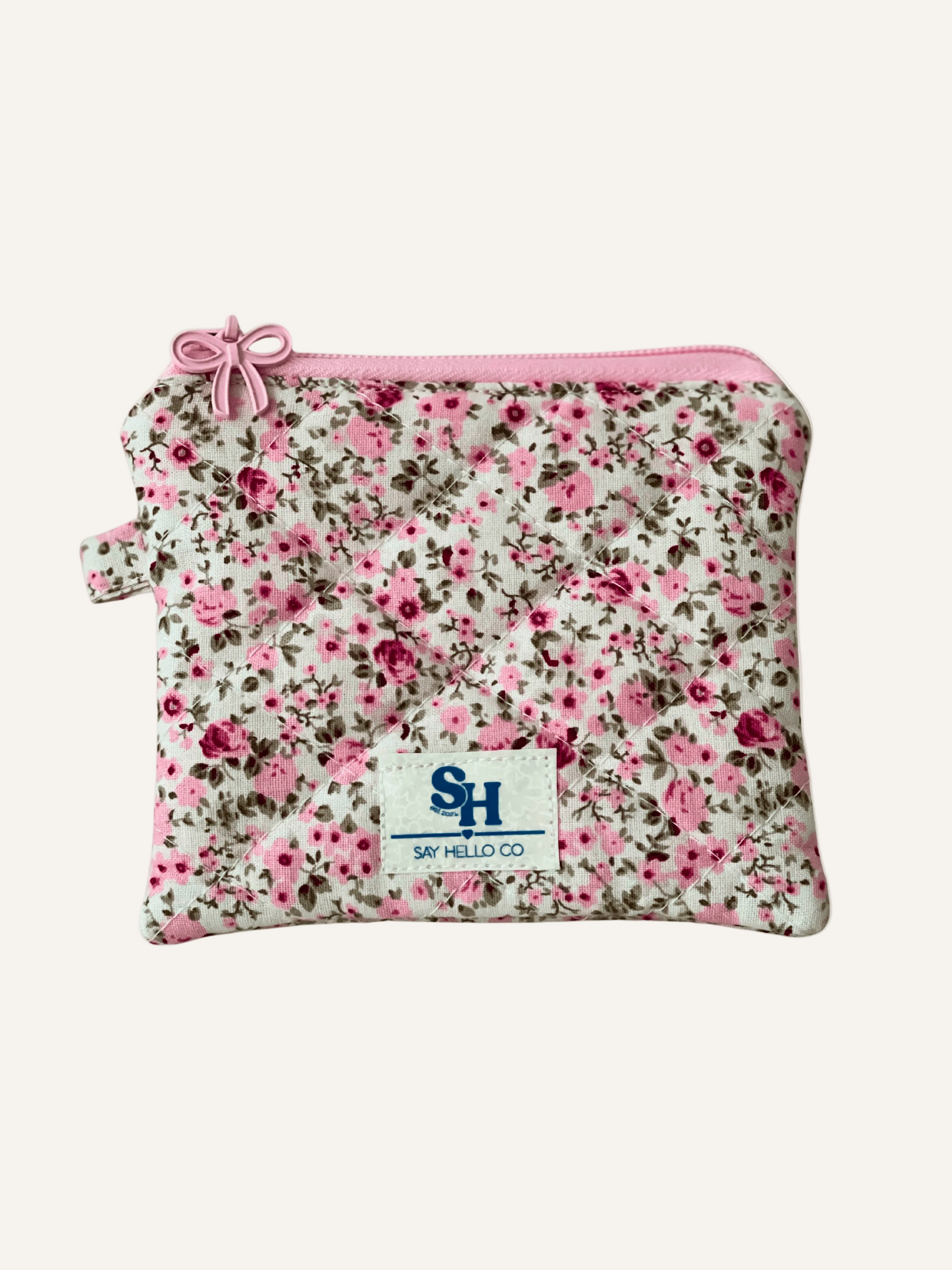Pink Floral-patterned pouch with a visible brand logo and a pink bow zipper on a warm cream background