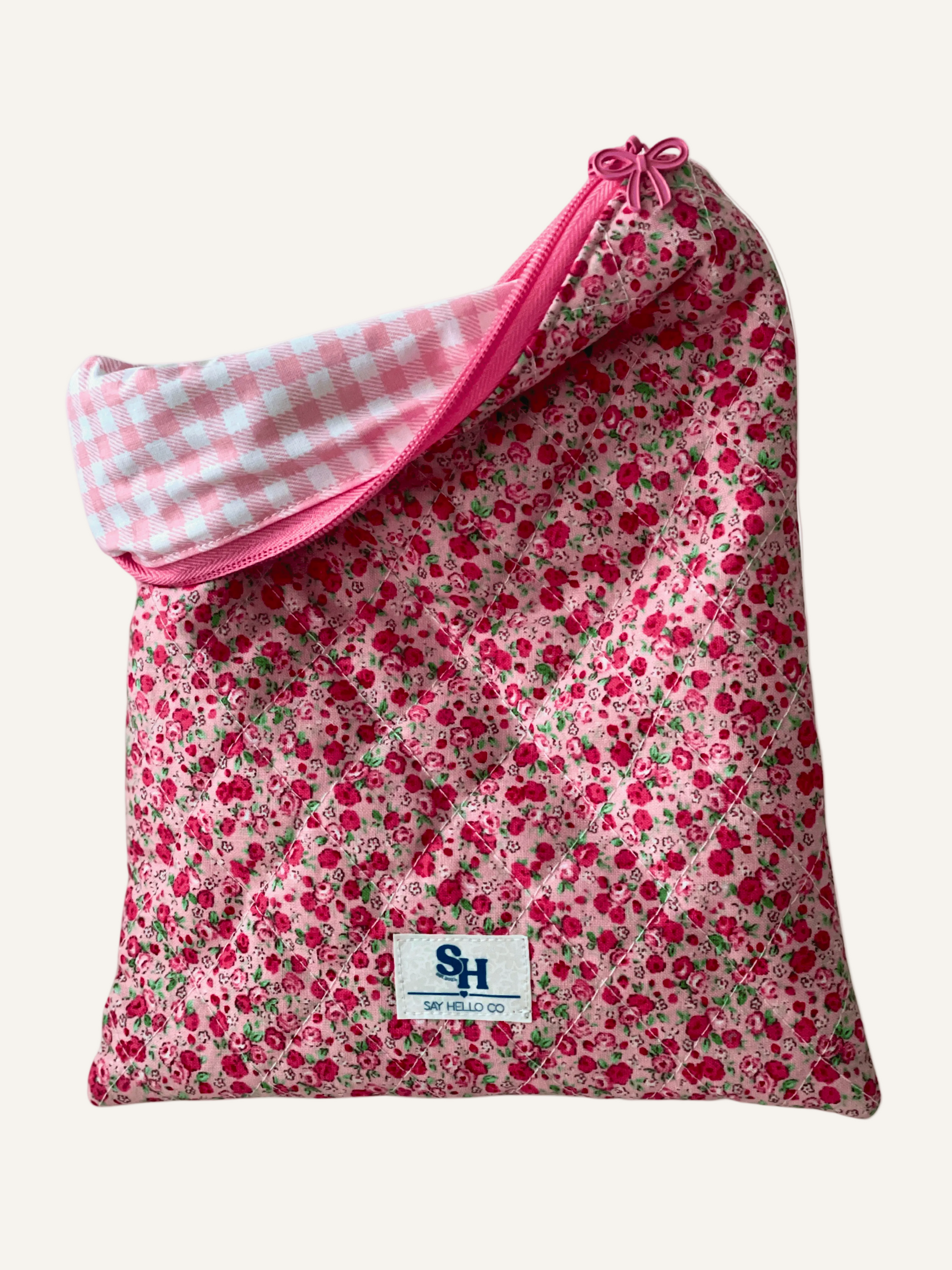 quilted book sleeve in a red and pink ditsy rose print with a pink checkered lining on a warm cream background